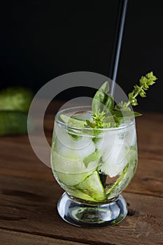 Cold fresh lemonade with cucumber, ice and mint leaves over wooden table and black background. Fresh summer drink in glass.