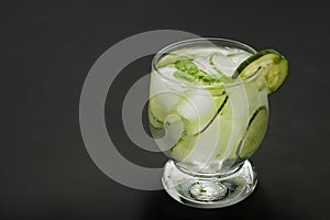 Cold fresh lemonade with cucumber, ice and mint leaves over wooden table and black background. Fresh summer drink in glass. Copy s