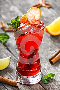 Cold fresh red lemonade with mint, orange, cinnamon and ice in glass on wooden background. Summer drinks