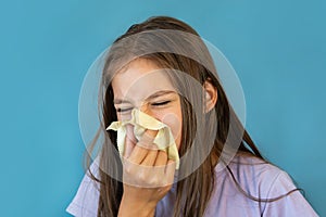 A cold girl blows her nose in a white rag on blue background. Influenza or Rhinitis snot runny nose stuffy nose. Allergy