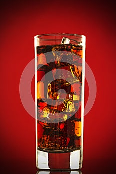 Cold glass of cola drink with ice cubes isolated on red background