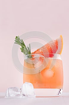 Cold grapefruit cocktail decorated twig rosemary and slice citrus closeup on pink background, vertical.