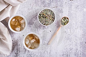 Cold green Japanese hojicha tea with ice in cups and dry tea in a bowl on the table. Top view