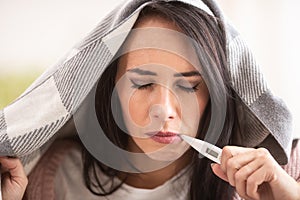 Cold having woman measures fever by holding thermometer in her mouth