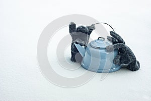 Cold and hot comparison with a teakettle and gloves in snow. Keeping warm and text space. photo