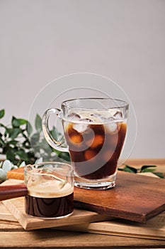 cold iced black brew coffee in a glass with pieces of ice on a wooden table, natural light, fresh summer drink