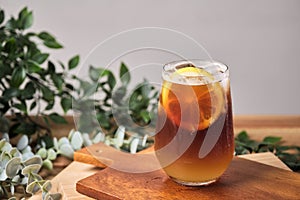 cold iced black brew coffee mixed lemon juice and lemon slices in a glass with pieces of ice on a wooden table, natural light,