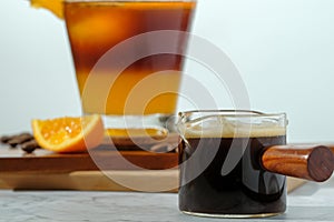 Cold Iced black coffee mixed with orange juice and orange slices in glass on wooden plate in white background with nature leaves