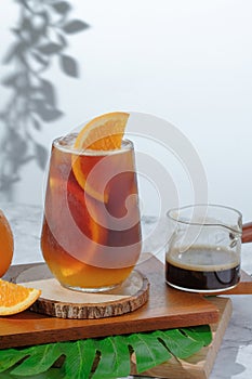 Cold Iced black coffee mixed with orange juice and orange slices in glass on wooden plate in white background with nature leaves photo