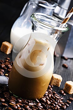 Cold iced coffee with milk and ice in a glass jug, dark background, selective focus