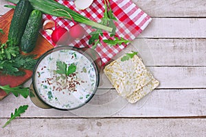 Cold kefir soup in glass bowl with spicy herbs, cucumber, radish