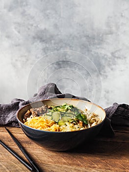 Cold Korean kuksi soup with vegetables, scrambled eggs, beef and noodles in a bowl and chopsticks on rustic wood background