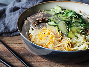 Cold Korean kuksi soup with vegetables, scrambled eggs, beef and noodles in a bowl and chopsticks on rustic wood background