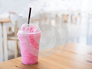 Cold milk smoothie in a plastic cup on a wooden table and has sunlight a beautiful background.