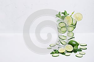 Cold mineral water with slices cucumber, lime, mint and ice on soft white background, copy space. Summer refreshing drinks.