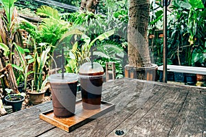 Cold mocha coffee in plastic cup on wooden table in cafe with plant and sunlight background. glass of Iced coffee with milk,