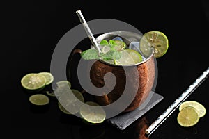 Cold Moscow Mule Alcoholic Cocktail in Copper Mug with Ice, Mint, and Lemon over Black Stone Table Background