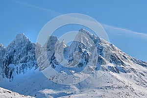 A cold mountain peak covered in snow during winter with a blue sky background. Beautiful landscape of a snowy summit