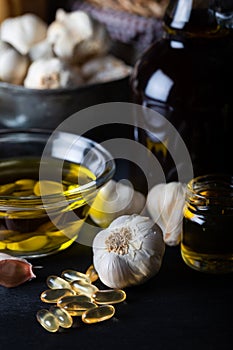 Cold pressed garlic oil in bowl with  garlic oil capsule on dark background.
