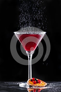 Cold red cocktail with red currant and powdered sugar in tall glass on black background. Summer drinks and alcoholic cocktails