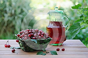 Cold refreshing drink from cherries in a pitcher and ripe berries in basket on wooden table
