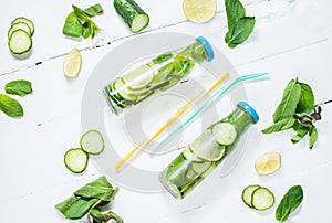 Cold and refreshing infused detox water with lime, mint and cucumber in a bottle on white wood background