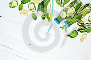 Cold and refreshing infused detox water with lime, mint and cucumber in a bottle on white wood background