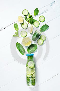 Cold and refreshing infused detox water with lime, mint and cucumber in a bottle on white wood background