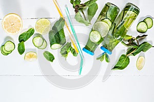 Cold and refreshing infused detox water with lime, mint and cucumber in a bottle on white wood background. Copyspace and