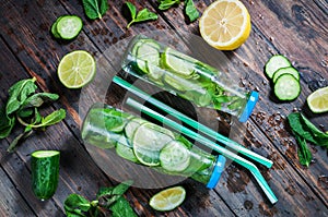 Cold and refreshing infused detox water with lime, mint and cucumber in a bottle on wood background