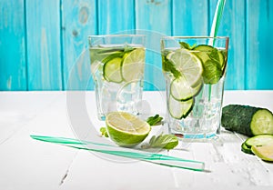 Cold and refreshing infused detox water with lime, mint and cucumber in a glass on wood background