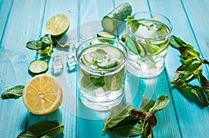 Cold and refreshing infused detox water with lime, mint and cucumber in a glass on wood background