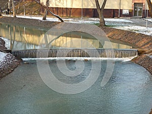 Cold river in the city park in winter, water flows down from the springboard
