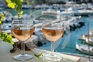 Cold rose wine in glasses served on outdoor terrace in sunlights with view on old fisherman`s harbour with colourful boats in