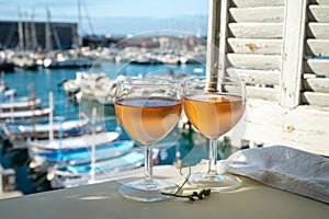 Cold rose wine in glasses served on outdoor terrace in sunlights with view on old fisherman`s harbour with colourful boats in