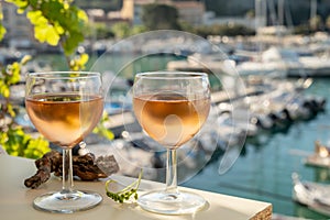 Cold rose wine in glasses served on outdoor terrace in sunlights with view on old fisherman`s harbour with colourful boats in