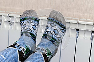 Cold season. Feet in socks on the battery. The concept of heat in the house.
