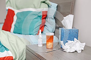 Cold season flue, virus illness. Pills, paper tissue, nasal spray, thermometer on table by bed in a bedroom. Medicine and health