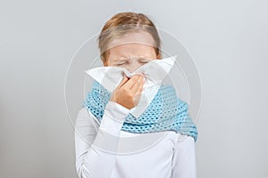 Cold season. Little girl in a warm scarf blows her nose. A child on a gray background