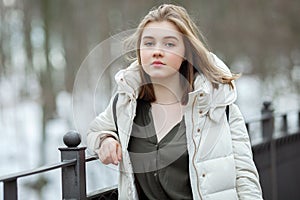 Cold season young beautiful woman in white coat with disheveled hair posing on park bridge lifestyle concept portrait