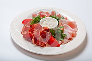 Cold smoked meat plate with prosciutto, salami, bacon, ham and sauce on a white plate.