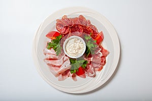 Cold smoked meat plate with prosciutto, salami, bacon, ham and sauce on a white plate.