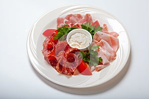 Cold smoked meat plate with prosciutto, salami, bacon, ham and sauce on a white plate.