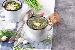 Cold Soup Okroshka in enamel cup and raw ingredients on grey stone table