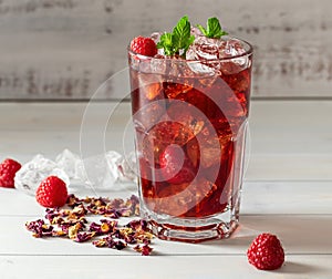 Cold sparkling hibiscus or karkade tea with lemon, mint, and ice in glass on a wooden table.