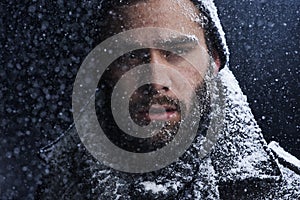 That cold stare could melt any heart. a serious young man covered in snow in the dark.