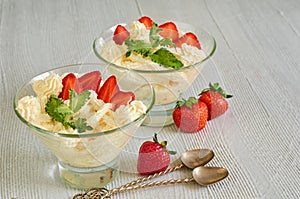 Cold summer dessert with sliced strawberries, cheese cream in the glass bowls on the gray kitchen table. Parfait with mint