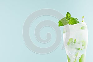 Cold summer healthy mint water with green leaves, ice cubes, soda, straw in misted glass on pastel green color background, closeup