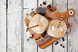 Cold summer iced coffee on a serving board, top view over white wood