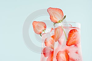 Cold summer strawberry water with strawberry slices, ice cubes, soda in misted glass on pastel green color background, closeup.